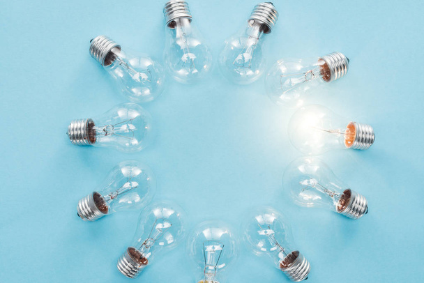 top view of light bulbs in circle and one of them glowing on blue background, having new idea concept - Foto, Bild