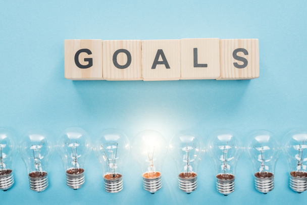 top view of glowing light bulbs under 'goals' word made of wooden blocks on blue background, goal setting concept - Foto, Bild