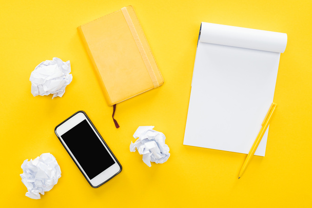 blank notebook, crumbled paper balls and smartphone with blank screen on yellow background - Photo, Image