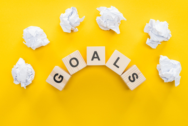 crumbled paper balls over 'goals' word made of wooden blocks on yellow background, goal setting concept - 写真・画像