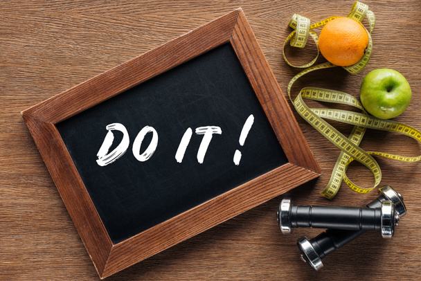 fruits, dumbbells, measuring tape and wooden chalk board with 'do it' quote, dieting and healthy lifesyle concept - Photo, Image