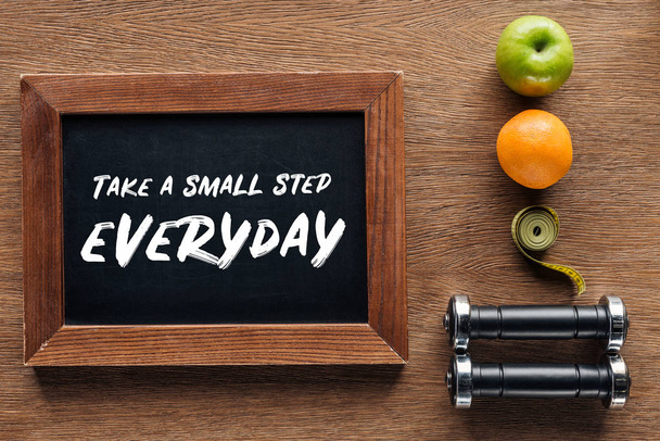 Obst, Hanteln, Maßband und hölzerne Kreidetafel mit Zitat "Jeden Tag einen kleinen Schritt machen", Diät und gesundes Lebensstilkonzept - Foto, Bild