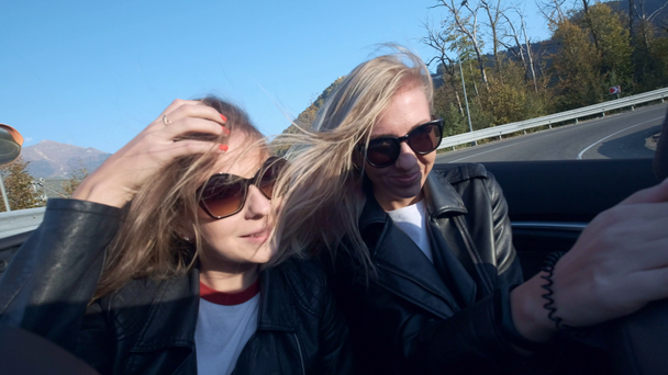 Twee mooie jonge stijlvolle meisjes rijden in een rode cabriolet op een achtergrond van bergen. Geniet van een vakantie in de bergen. - Video