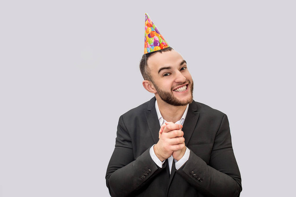 Happy and excited young man keeps hands together. He looks on camera and smile. Guy wears festive cone on head. Isolated on white background. - Φωτογραφία, εικόνα