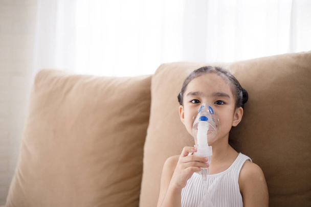 Söpö aasialainen lapsi potilaan inhalaatiohoito inhalaattorin naamiolla pehmeällä virtaussavulla keuhkoputkia laajentavasta aineesta
. - Valokuva, kuva