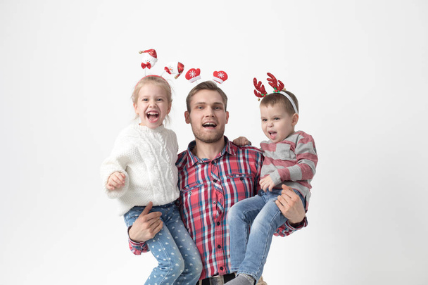 Father holds children in his arms on a white background. Happy family in funny Christmas headbands. - Foto, Imagen