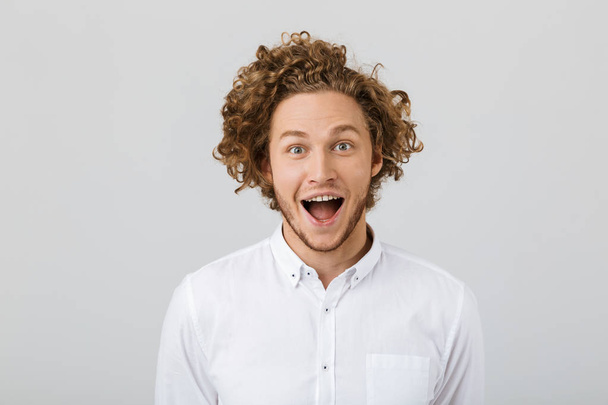 Portrait of a surprised young man with curly hair isolated over white background, open mouth - Fotó, kép