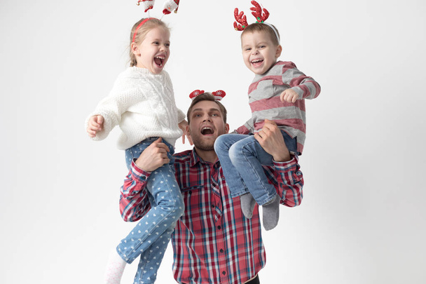 Father holds children in his arms on a white background. Happy family in funny Christmas headbands. - Fotoğraf, Görsel