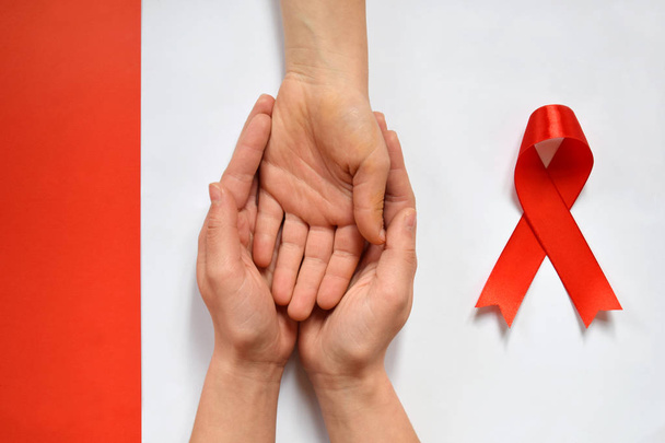 Patient support with diagnosis of HIV AIDS. Womens hands holding hand on white background. World Aids Day and red ribbon. Bad news lessening, trust and ethics concept - Foto, afbeelding