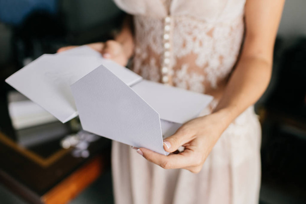 Female bride in white dress, holds white letter or envelope, prepares for invitation, prepares for wedding ceremony. Marriage concept - Photo, Image