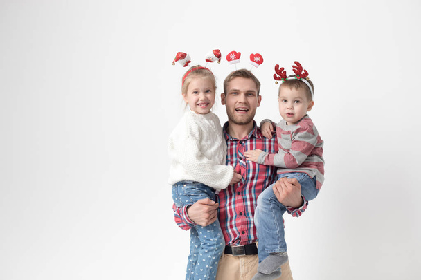 Father holds children in his arms on a white background. Happy family in funny Christmas headbands. - Φωτογραφία, εικόνα