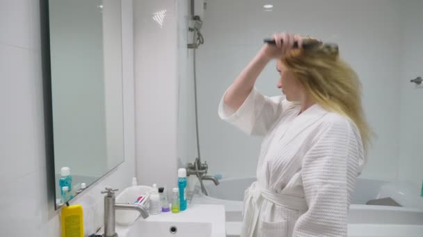 髪の健康の概念。コーミング彼女のブロンドの女性が浴室で乾燥した髪を破損しています。. - 映像、動画