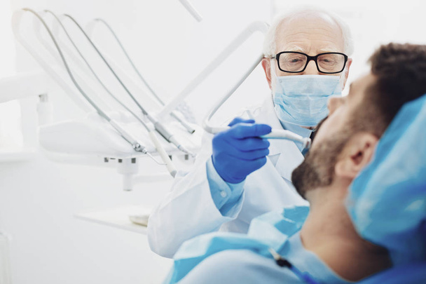 Concentrated male dentist removing teeth decay - Foto, afbeelding