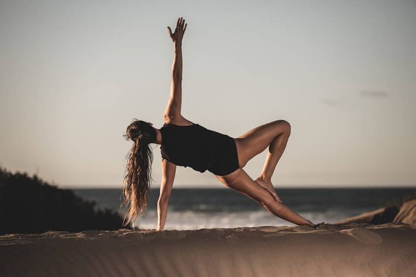 Вид сзади женщины, занимающейся доской асана на боковой тренировке йоги на песчаном пляже при солнечном свете
 - Фото, изображение