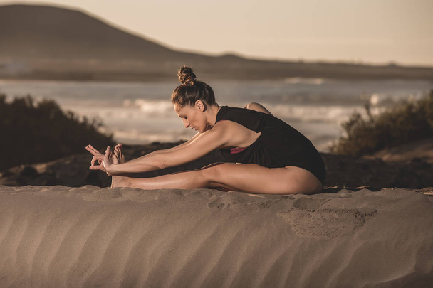 A koncentrált fiatal nő ül a homok és a jóga, a béke és a napfény oldalnézete - Fotó, kép