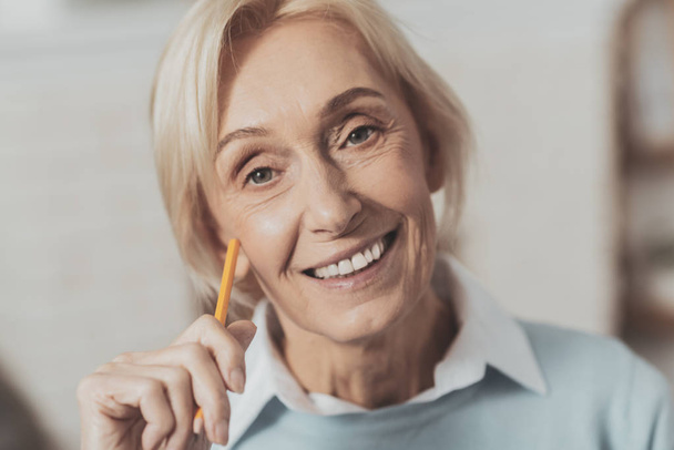Facial expression. Portrait of a happy aged woman while holding a pencil - Photo, Image