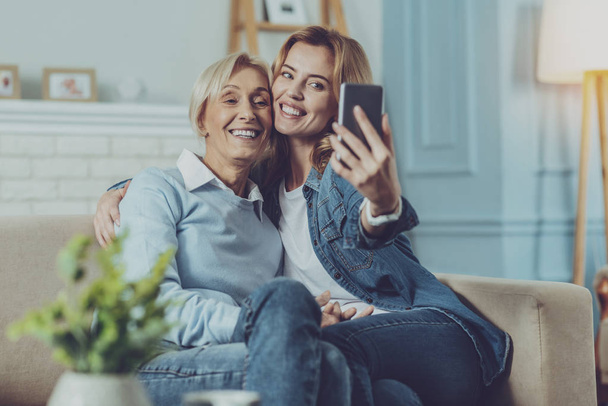 Elderly lady sitting with her daughter and making selfie - Foto, imagen