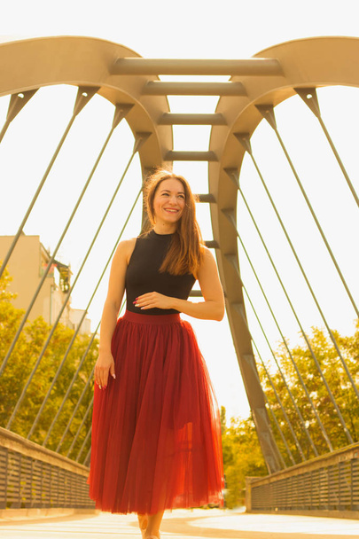 Young slim beautiful woman with long brown hair dancing and smiling outdoors in black shirt and terracotta (red pear) long skirt. Sport and healthy concept. - Фото, зображення
