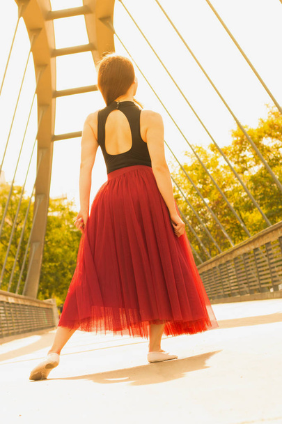 Young slim beautiful woman with long brown hair dancing and smiling outdoors in black shirt and terracotta (red pear) long skirt. Sport and healthy concept. - Foto, Imagen