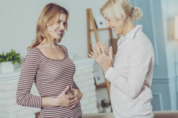 Positive woman looking at the belly of her pregnant daughter - Foto, Bild