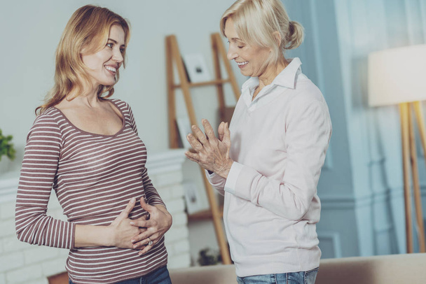 Senior woman looking at pregnant daughter with a smile - Foto, imagen