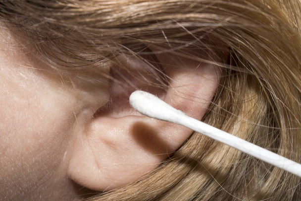 A woman cleans her ears with a cotton swab.Background man cleans ears. - Photo, Image
