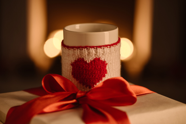 present and knitted mug with heart symbol on blurred background - 写真・画像