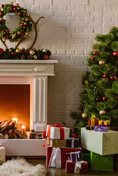 christmas tree with festive decorations and gift boxes near fireplace with firewood in living room - Photo, image