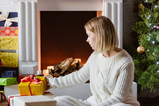 jeune femme mettant boîte cadeau près de la cheminée avec du bois de chauffage
 - Photo, image