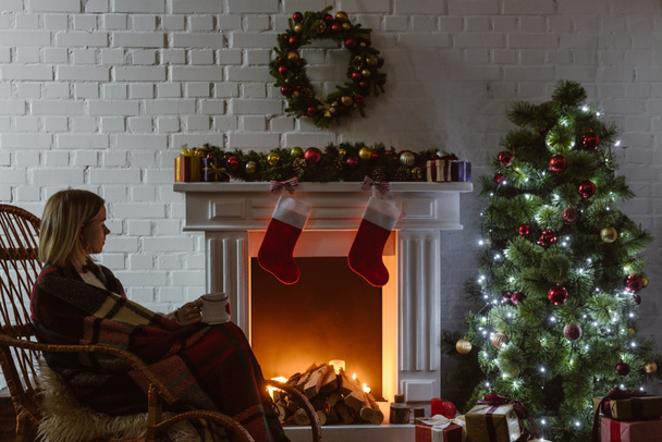  mujer joven en mecedora de mimbre sosteniendo taza de café en la sala de estar decorada para Navidad
  - Foto, imagen