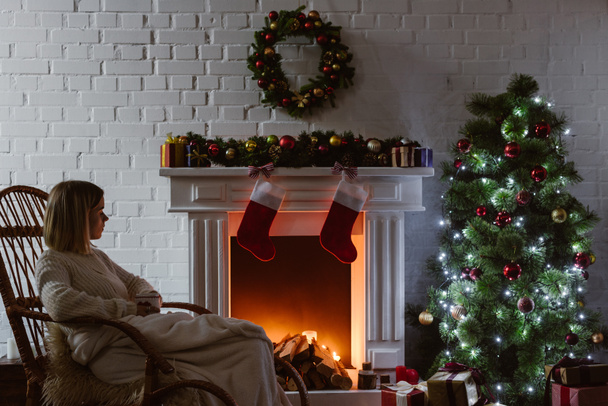  young woman sitting on wicker rocking chair in living room decorated for christmas  - Photo, Image