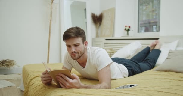 Young guy in pajamas reading a book in the bed , in the evening. - Filmmaterial, Video