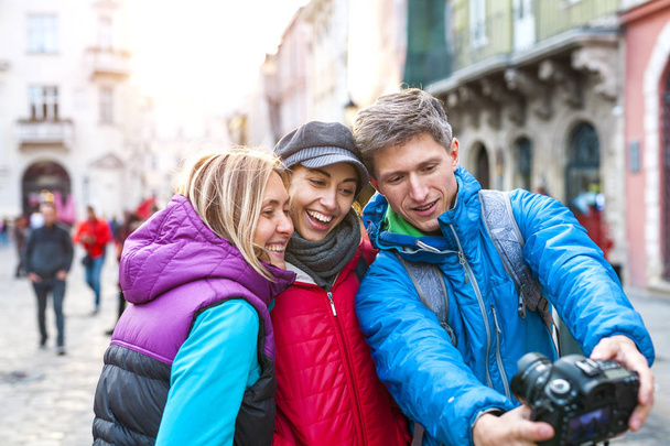Φίλοι πάρει μια selfie. Τρεις φίλοι περπατώντας στην όμορφη παλιά πόλη. Ταξίδια σε πόλεις της Ευρώπης. Δύο γυναίκες και έναν άνδρα φωτογραφίζονται με φόντο των παλαιών κτιρίων. - Φωτογραφία, εικόνα