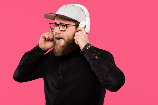 bearded male hipster listening music in headphones isolated on pink - Фото, изображение