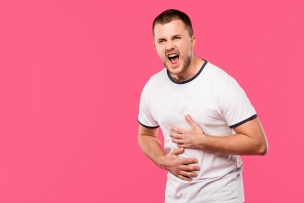 angry man yelling and having stomach pain isolated on pink - Foto, Imagem