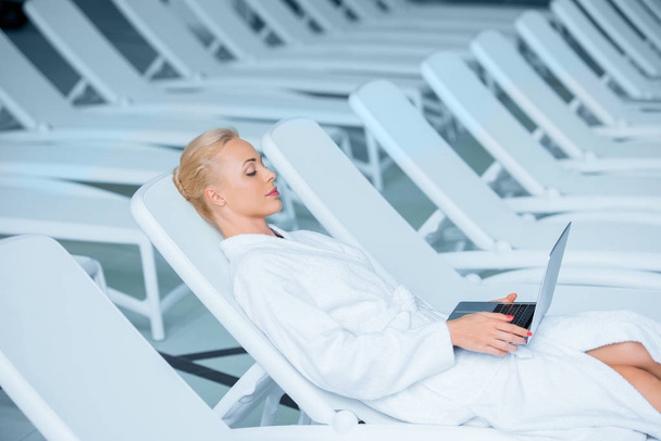  Όμορφη γυναίκα ξαπλωμένη σε ξαπλώστρα με φορητό υπολογιστή  - Φωτογραφία, εικόνα