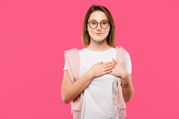 stylish girl in eyeglasses holding hands on chest isolated on pink - Photo, Image