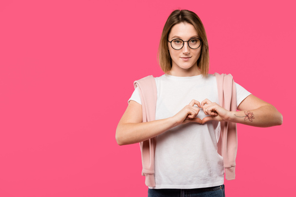 stylish girl in eyeglasses showing heart symbol isolated on pink - 写真・画像