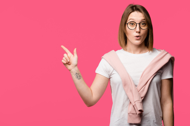 surprised young woman in eyeglasses pointing by finger isolated on pink - Foto, Bild