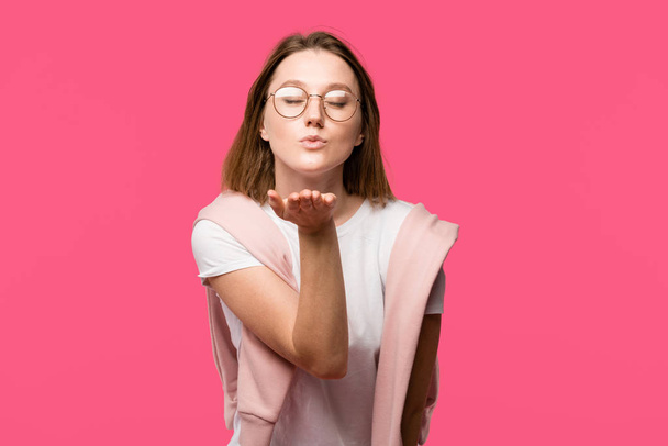 beautiful young woman with closed eyes blowing air kiss isolated on pink - Zdjęcie, obraz