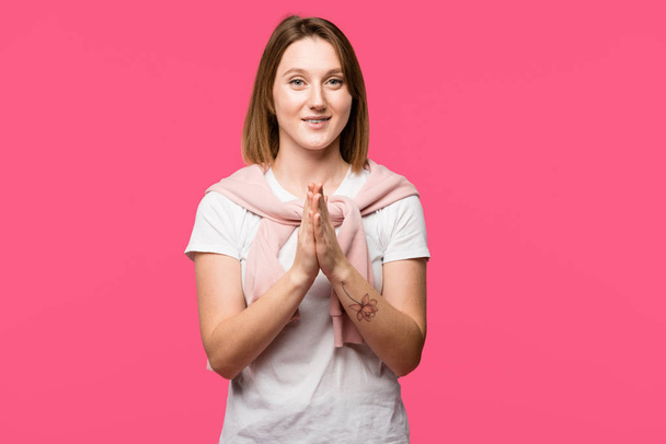 joyful young woman looking at camera with hand palms together isolated on pink - Fotoğraf, Görsel