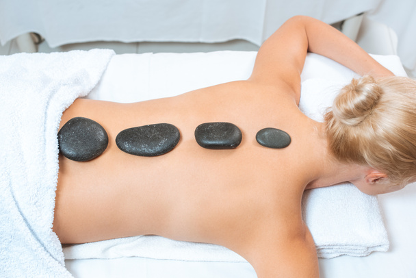 Dos de femme blonde avec des pierres chaudes sur la table de massage
 - Photo, image