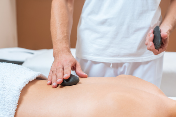 Close up de massagista masculino colocando pedras quentes na mulher de volta
  - Foto, Imagem