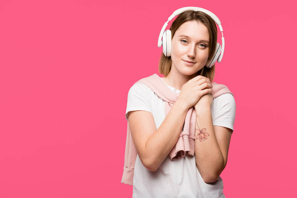 dreamy girl in headphones listening music and looking at camera isolated on pink - Foto, Imagem