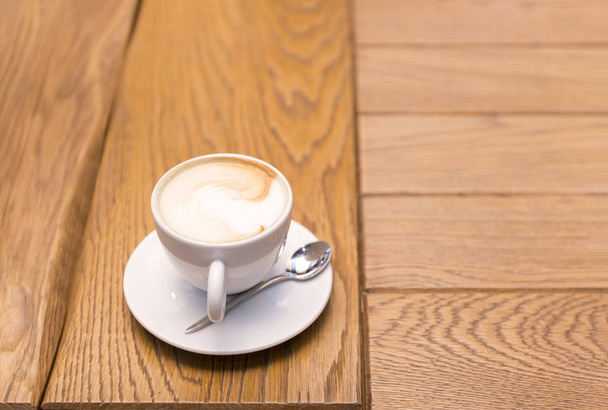 Cup of coffee on a wooden table, a teaspoon, a cappuccino in a white Cup on a white saucer - Foto, afbeelding