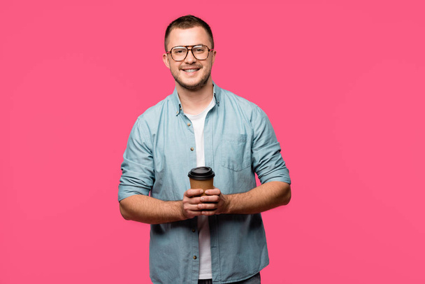 handsome happy man holding coffee to go and smiling at camera isolated on pink - Foto, Bild