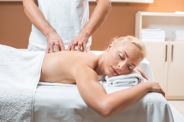 blonde woman lying with closed eyes while man doing massage - Photo, Image