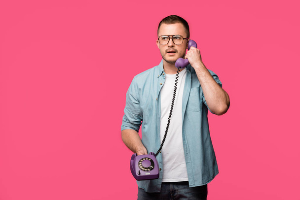 serious young man in eyeglasses talking by vintage telephone isolated on pink - Φωτογραφία, εικόνα