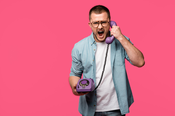 emotional young man yelling at handset and looking at camera isolated on pink - Фото, зображення