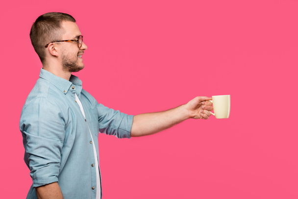 side view of smiling man holding mug and looking away isolated on pink - Foto, afbeelding